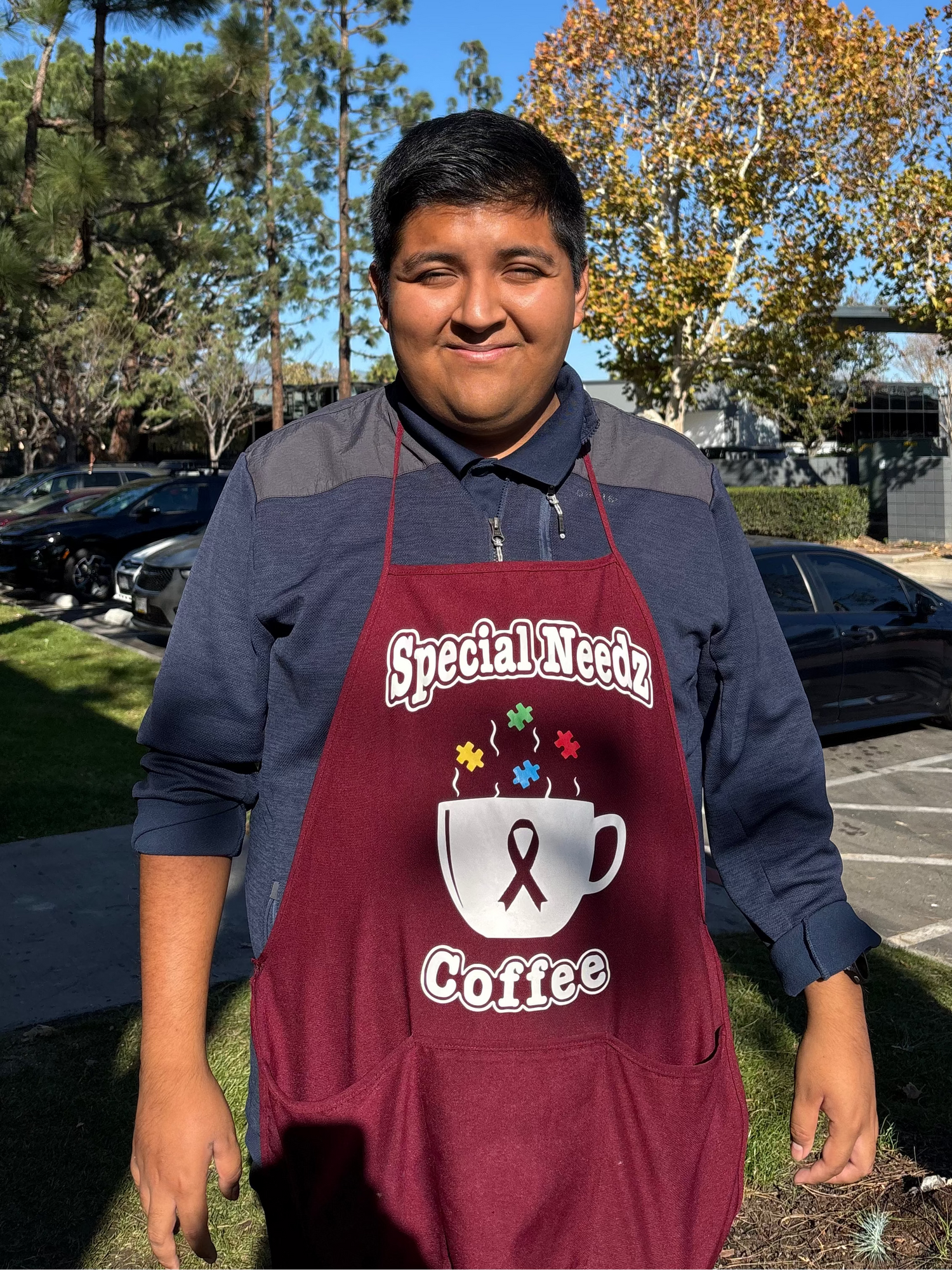 Person wearing a maroon apron with 'Special Needz Coffee' text and graphics outdoors.